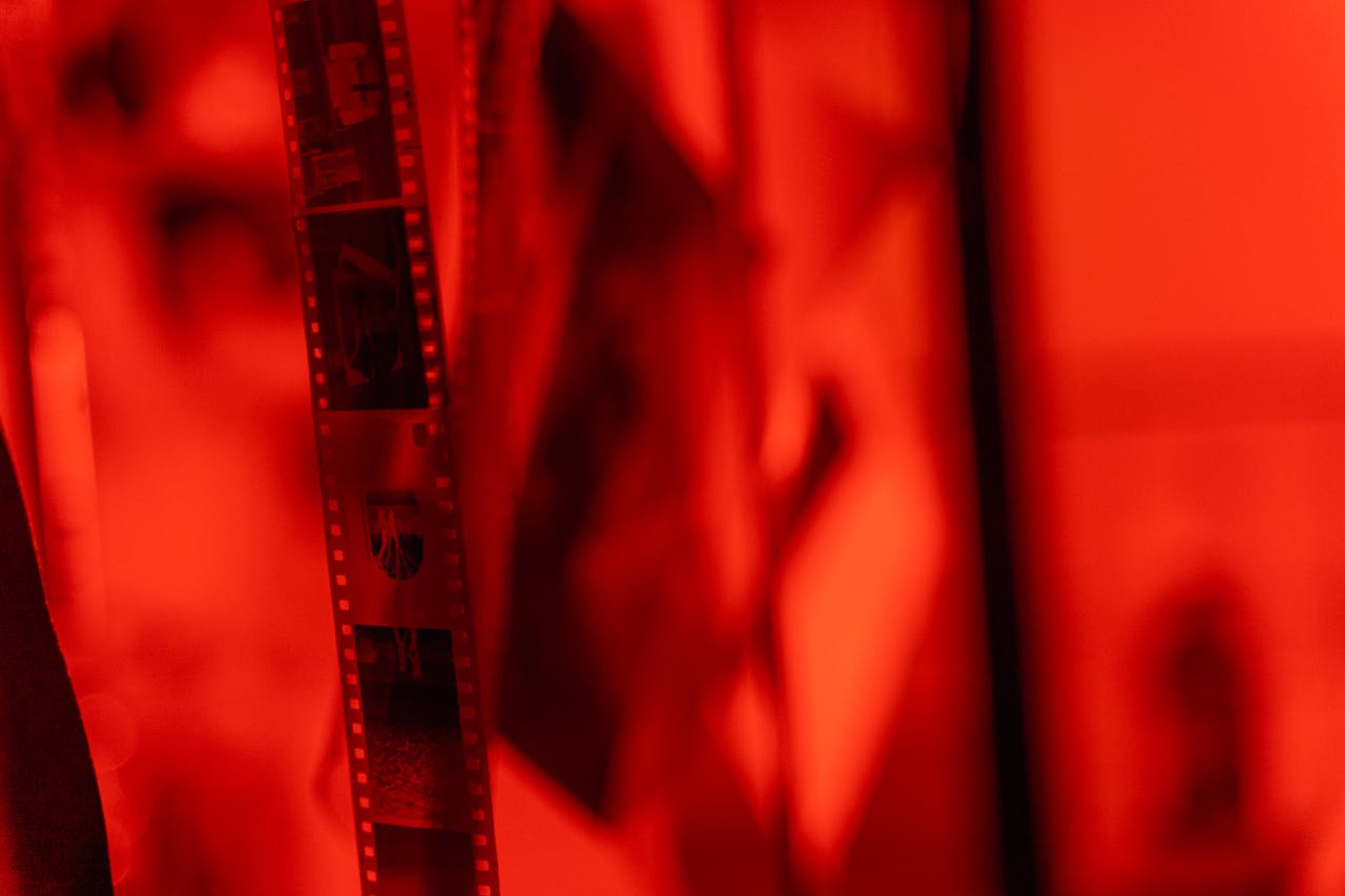 Close-up view of film negatives hanging in a darkroom under red lighting.